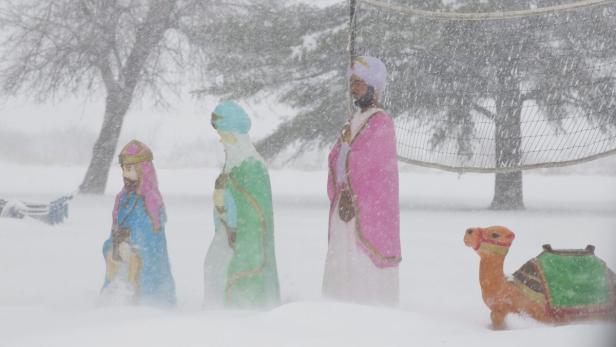 Krippenfiguren der Heiligen Drei Könige und ein Kamel stehen im Schnee.