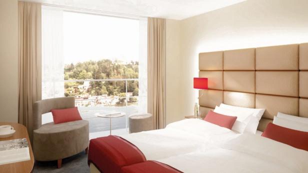 Ein helles Hotelzimmer mit Blick auf einen See und grüne Hügel.