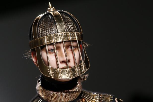 Ein Model trägt einen goldenen, käfigartigen Kopfschmuck mit Nieten.