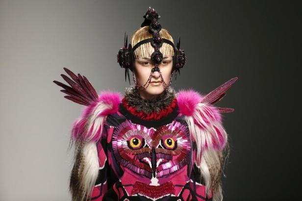 Ein Model präsentiert ein extravagantes Outfit mit Federn und einem Eulenmotiv.