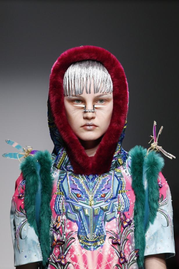 Ein Model mit silberner Stirnfranse und aufwendigem, farbenfrohem Kostüm mit Fellbesatz.