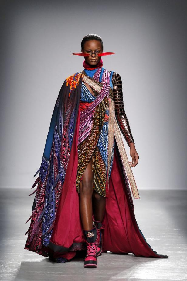 Eine Frau in einem farbenprächtigen, extravaganten Kleid auf einem Laufsteg.