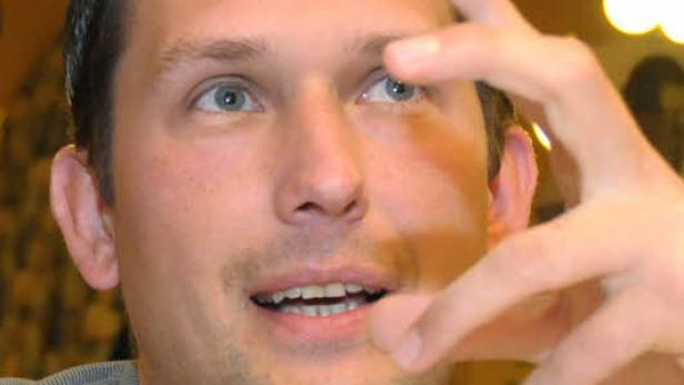 Ein Mann mit hellen Augen gestikuliert mit der Hand vor seinem Gesicht.
