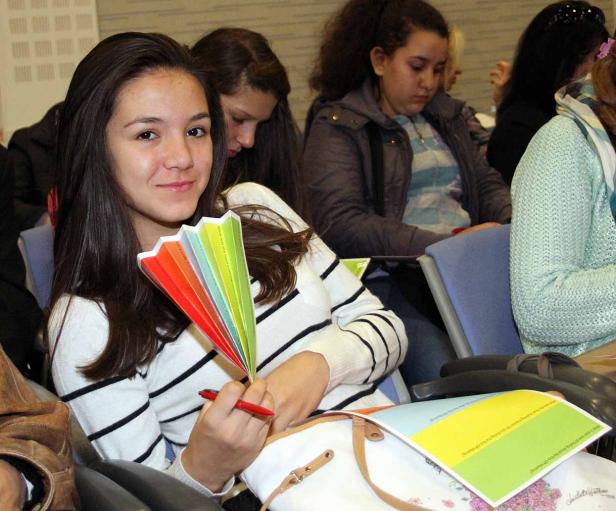 Ein junges Mädchen sitzt mit einem bunten Fächer und einem Stift in der Hand.
