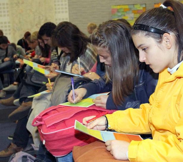 Eine Gruppe Schüler sitzt in einem Raum und bearbeitet farbige Blätter.