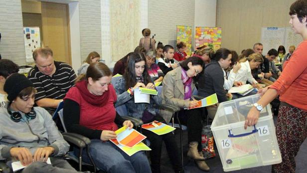 Eine Gruppe von Menschen sitzt in einem Raum und arbeitet mit farbigen Papierbögen.