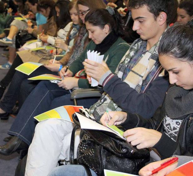 Mehrere Personen sitzen in einer Reihe und füllen Papiere aus.