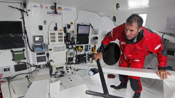 Ein Mann in roter Segelbekleidung in einem Schiffsinneren mit zahlreichen Instrumenten.