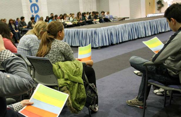 Zuschauer sitzen bei einer Präsentation mit farbigen Blättern im Publikum.