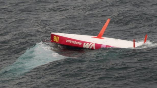 Ein gekentertes Segelboot mit der Aufschrift „VM Matériaux“ treibt im Wasser.