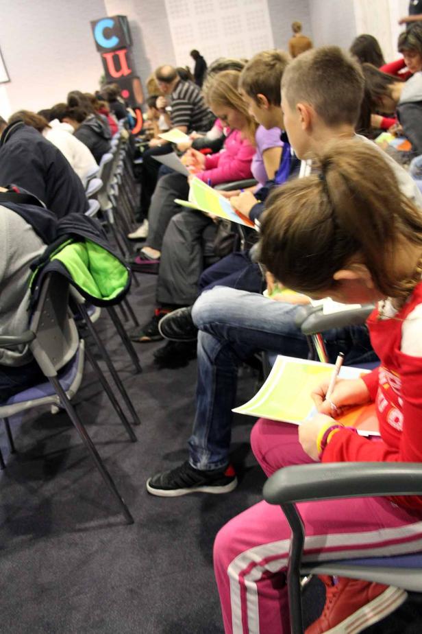 Kinder sitzen in einem Raum und schreiben oder zeichnen auf Papier.