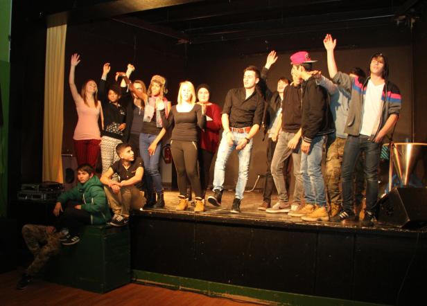 Eine Gruppe junger Leute steht auf einer Bühne und winkt ins Publikum.