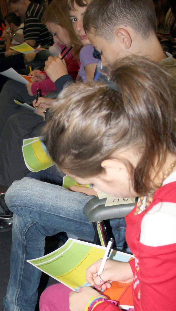 Mehrere Kinder sitzen und schreiben oder zeichnen auf Papier.