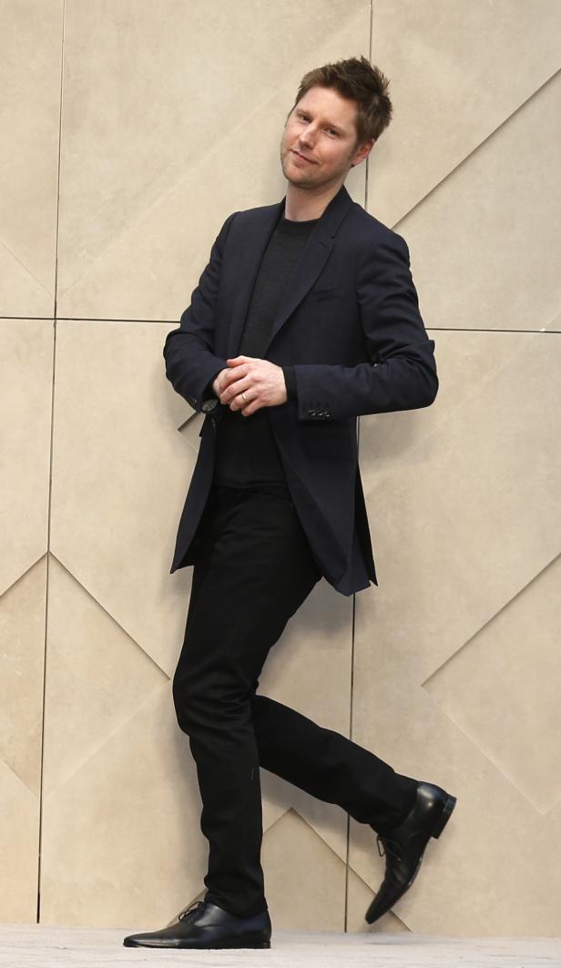 Ein Mann in Anzug posiert vor einer Wand mit geometrischem Muster.