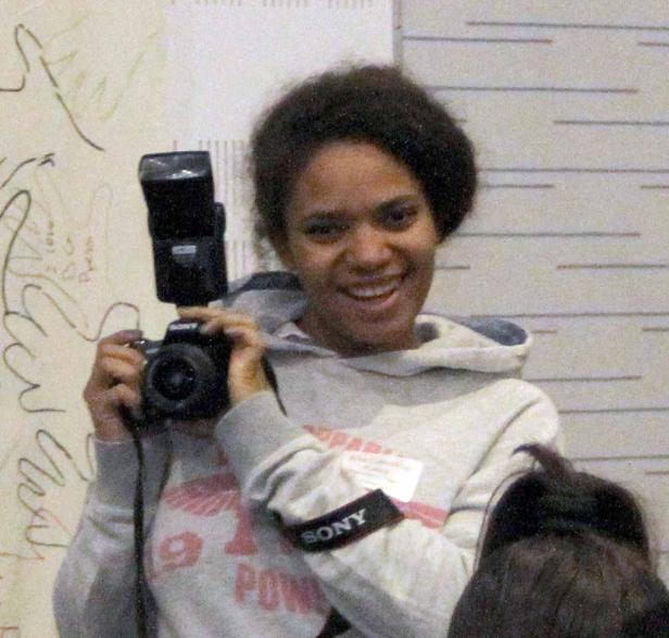 Eine lächelnde junge Frau fotografiert mit einer Sony-Kamera mit Blitz.