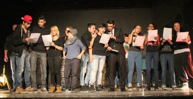 Eine Gruppe junger Leute steht auf einer Bühne und liest von Blättern ab.