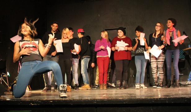 Eine junge Frau performt auf einer Bühne vor einer Gruppe von Menschen.