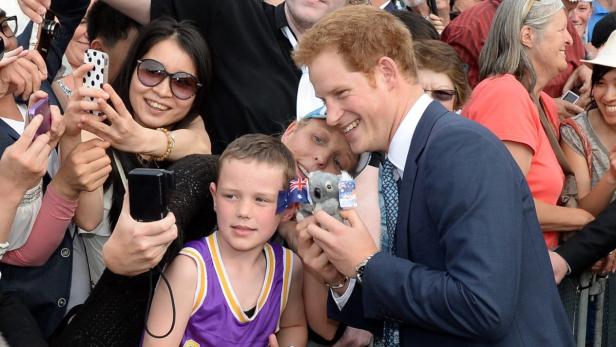 Prinz Harry umringt von Fans, hält einen Koala-Bären mit australischen Flaggen.