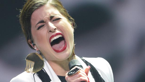 Eine Sängerin mit rotem Lippenstift singt mit weit geöffnetem Mund in ein Mikrofon.