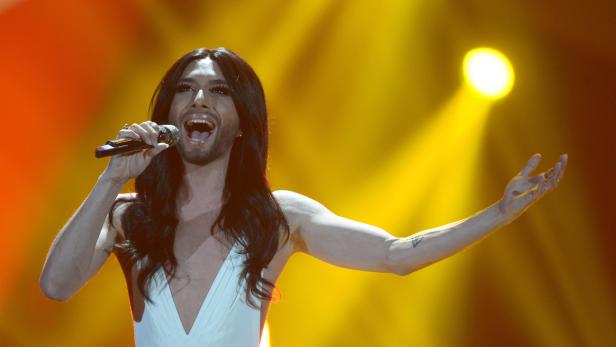 Conchita Wurst singt mit einem Mikrofon in der Hand auf einer Bühne.