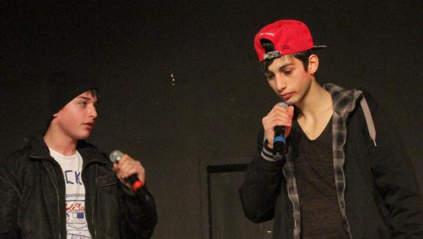 Zwei junge Männer stehen mit Mikrofonen auf einer Bühne.
