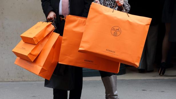 A couple walk with Hermes shopping bags as they le Zwei Personen tragen mehrere orangefarbene Einkaufstaschen von Hermès.