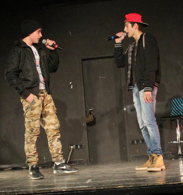 Zwei junge Männer rappen auf einer Bühne in Mikrofone.