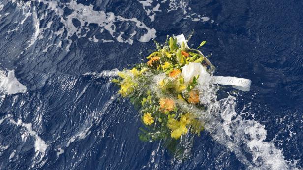Fischer warfen am Samstag Blumengebinde ins Meer. Ein Blumenstrauß treibt im blauen Wasser.