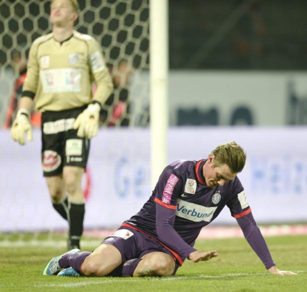 Ein Fußballspieler liegt enttäuscht auf dem Rasen, im Hintergrund ein Torwart.