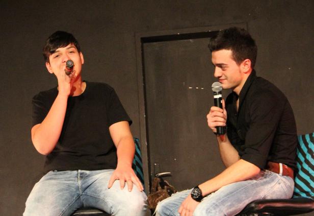 Zwei junge Männer sitzen auf Stühlen und sprechen in Mikrofone.