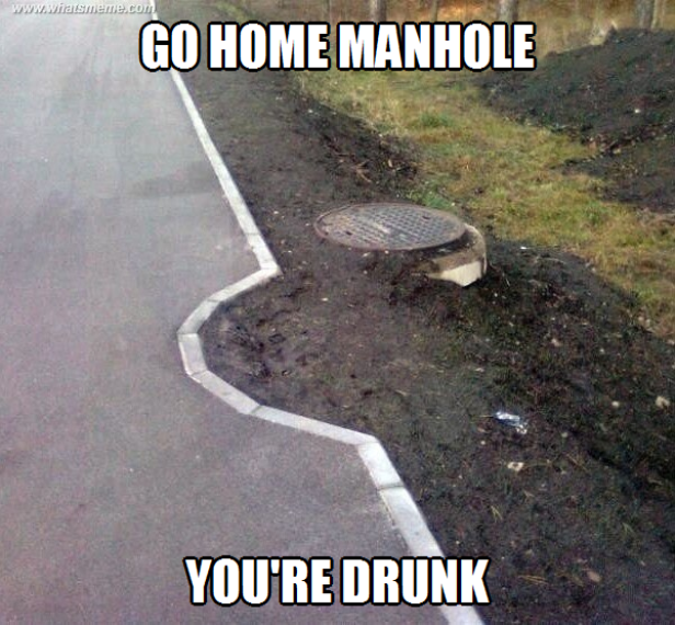 Ein Kanaldeckel liegt schief auf einem Erdhügel neben einem Gehweg.