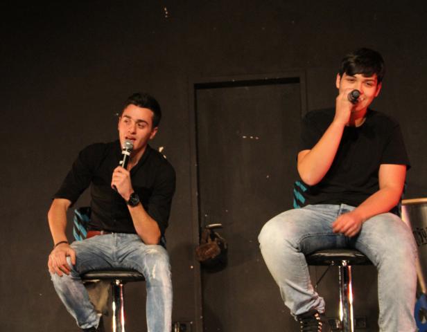 Zwei junge Männer sitzen auf Barhockern und singen in Mikrofone.