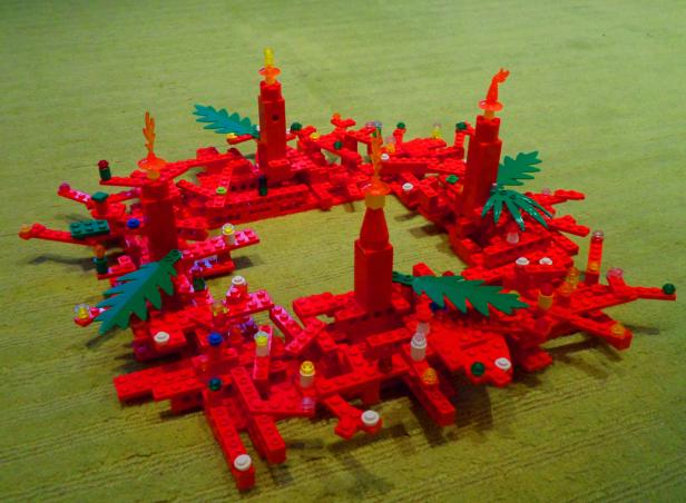 Ein Adventskranz aus roten Legosteinen mit grünen Blättern und Kerzen.