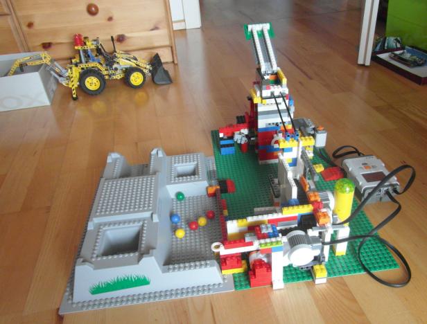 Eine Lego-Fabrik mit Kran, Förderband und einem gelben Bagger im Hintergrund.