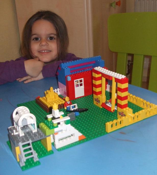 Ein Mädchen betrachtet ein Lego-Bauernhof-Set auf einem blauen Tisch.