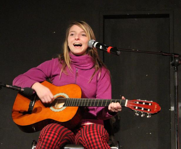 Eine junge Frau singt und spielt Gitarre auf einer Bühne.