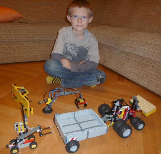 Ein Junge sitzt auf dem Boden, umgeben von Lego-Technik-Modellen.