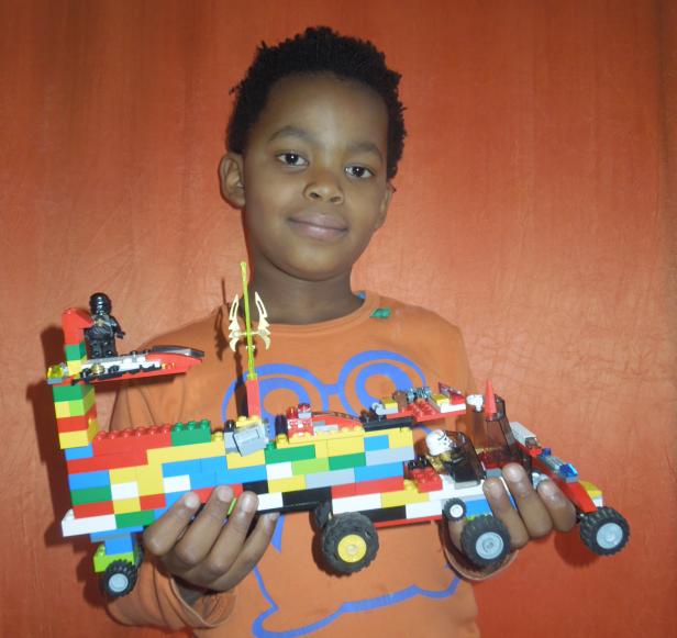 Ein Junge hält ein buntes Spielzeugauto aus Legosteinen in den Händen.