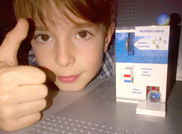 Ein Junge zeigt den Daumen nach oben neben einem „Murmelomat“ aus Legosteinen.