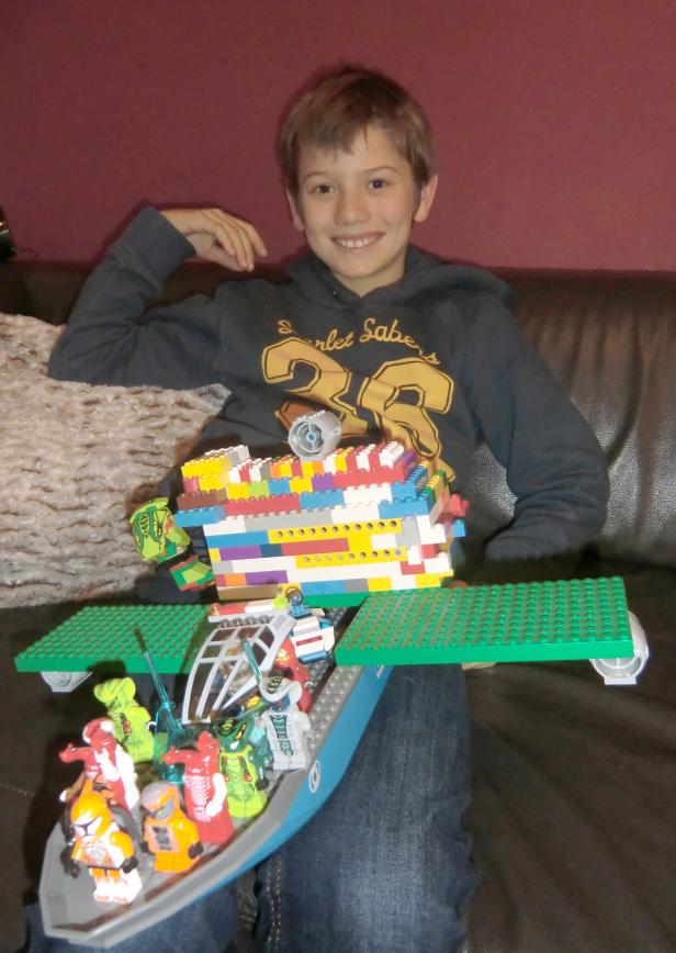 Ein lächelnder Junge präsentiert stolz sein selbstgebautes Lego-Raumschiff.