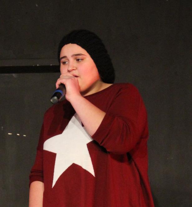 Eine junge Frau mit Mütze singt in ein Mikrofon.