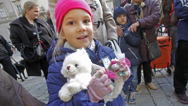 Ein lächelndes Mädchen mit rosa Mütze hält einen Teddybären und eine Handpuppe.