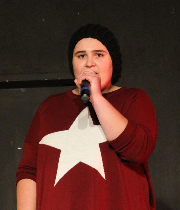 Eine junge Frau mit Mütze singt in ein Mikrofon.