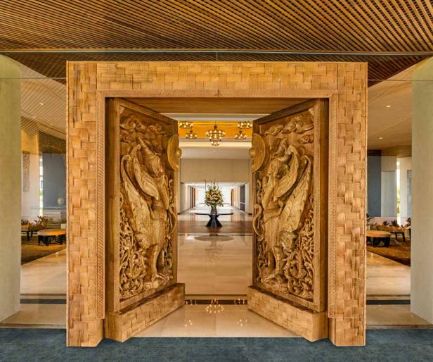 Eine kunstvoll geschnitzte Holztür mit mythologischen Figuren führt in einen luxuriösen Hotellobbybereich.