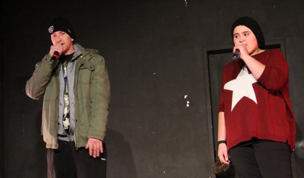 Zwei Personen stehen auf einer Bühne und singen in Mikrofone.