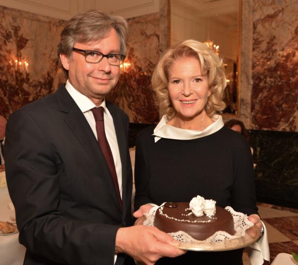 Ein Mann im Anzug und eine Frau halten gemeinsam eine Schokoladentorte.
