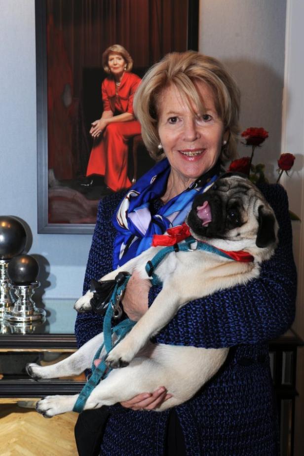Eine Frau hält einen Mops vor einem Porträt von sich selbst.