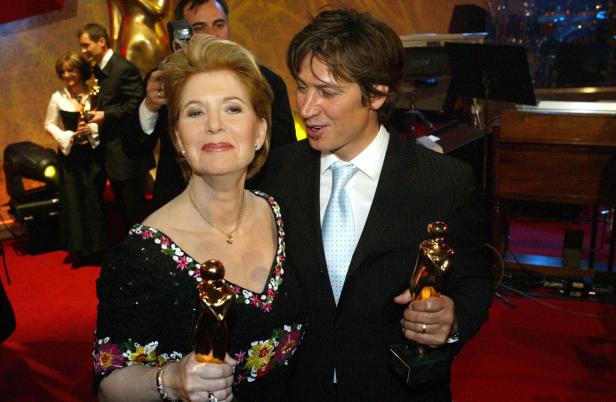 Eine Frau und ein Mann halten jeweils eine goldene Statue in der Hand.