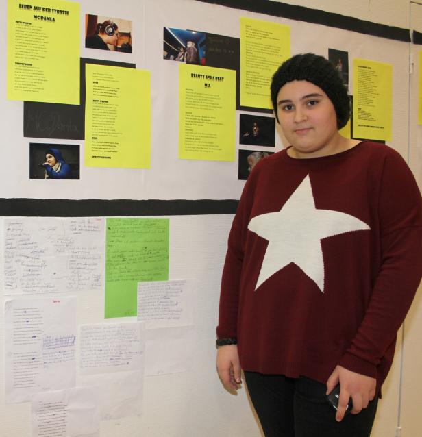 Eine Person steht vor einer Wand mit Texten und Fotos, möglicherweise im Kontext eines Musikprojekts.