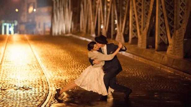 Ein Paar tanzt Tango auf einer beleuchteten Brücke bei Nacht.